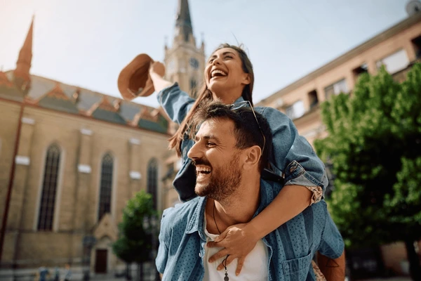 Happy couple enjoying a piggyback ride outdoors in front of a historic church building.