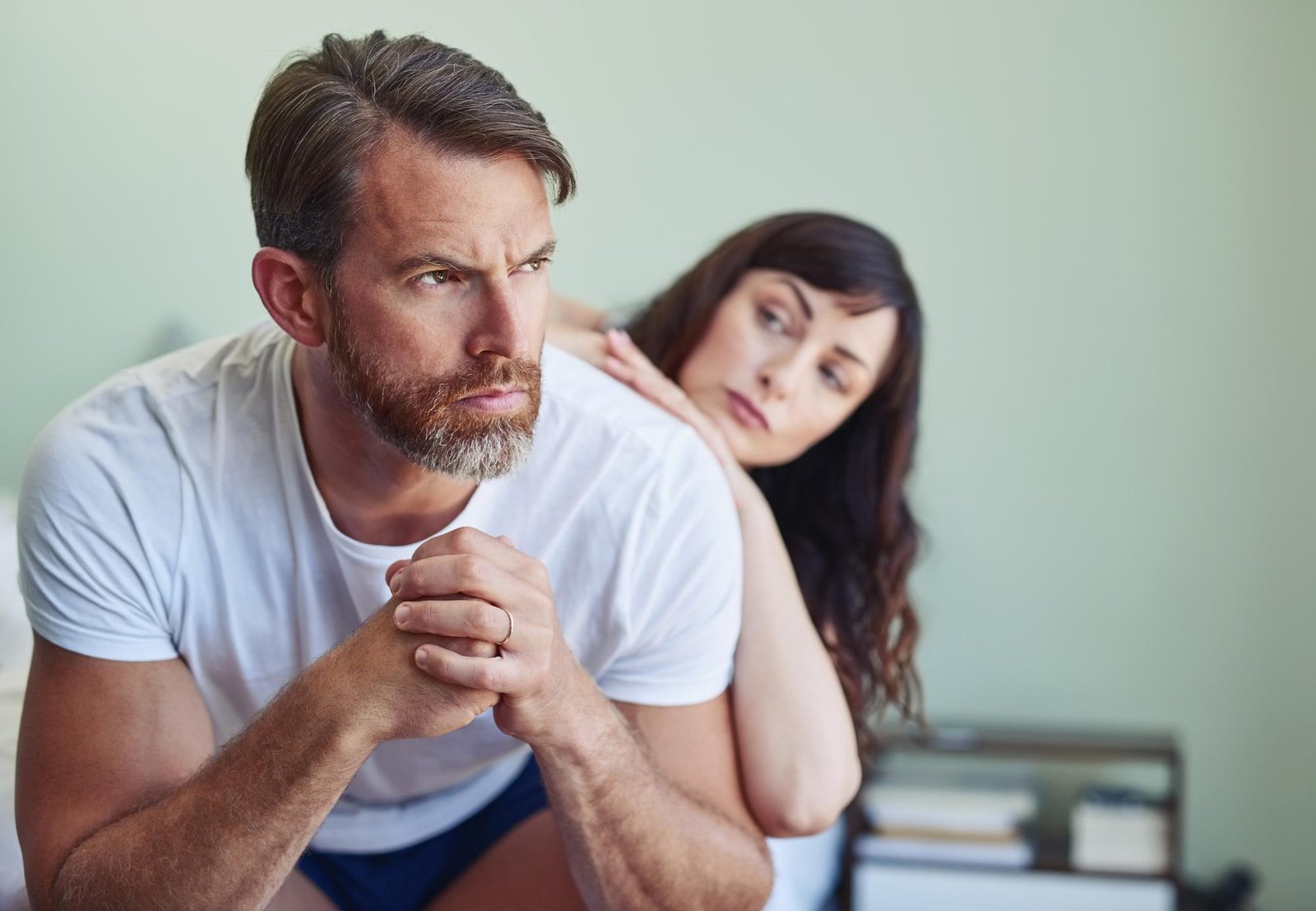 Worried husband sits on the bed while his wife leans on him, capturing the emotional distance and hidden tension of living with a covert narcissist partner.