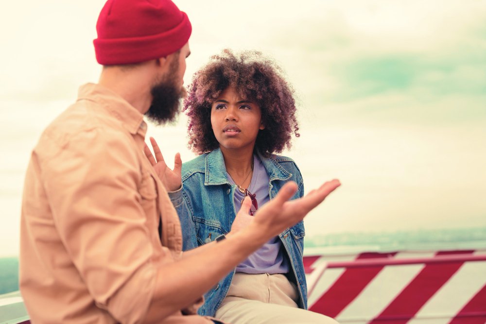 A man in a red beanie gestures while the woman crosses her arms, annoyed, showing what to do when your husband calls you names.