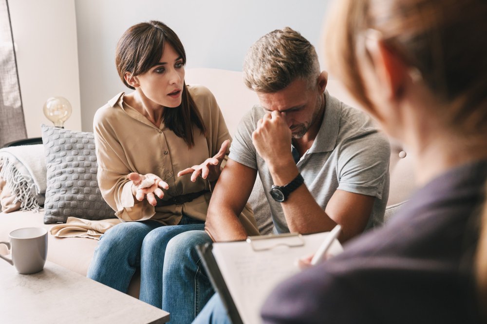 A distressed couple discussing emotional affair recovery with a therapist, showing the pain and confusion common during the early stages of healing after infidelity.