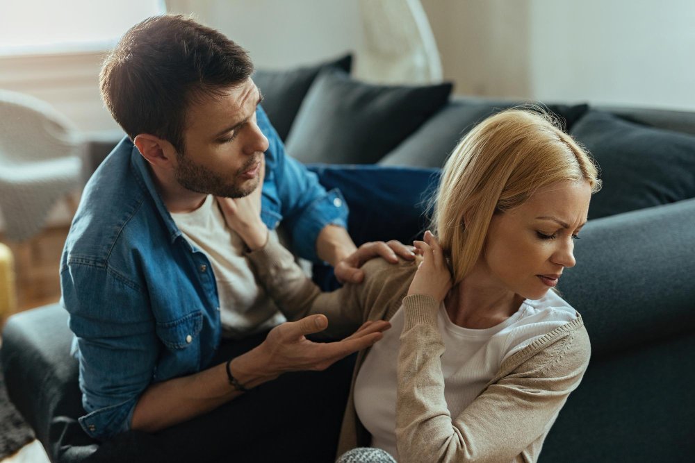 Woman sitting at home with arms crossed, looking away from her partner during a tense conversation.