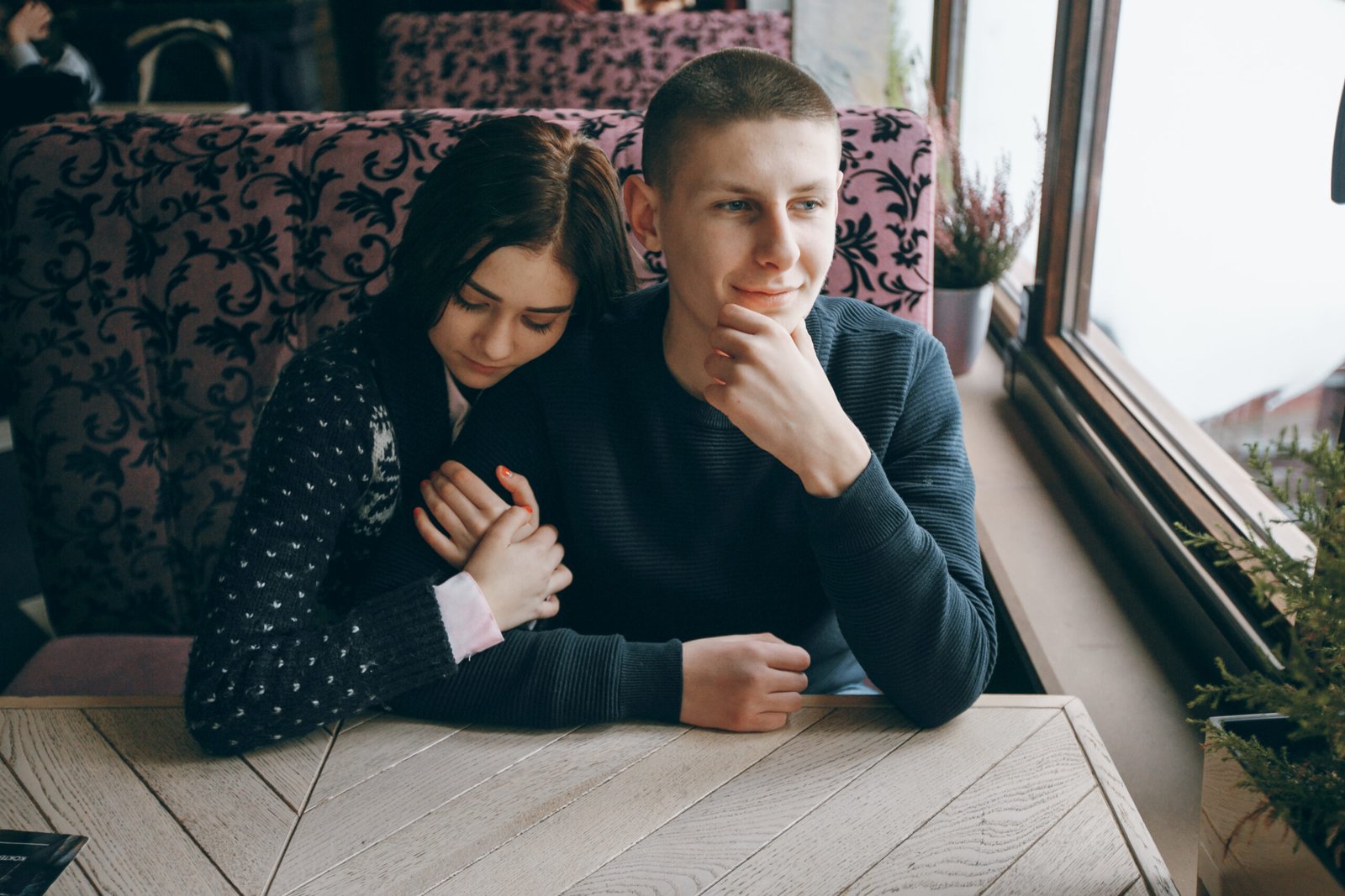 a couple at dinner, the woman holding her husband's arm while he looks out the window