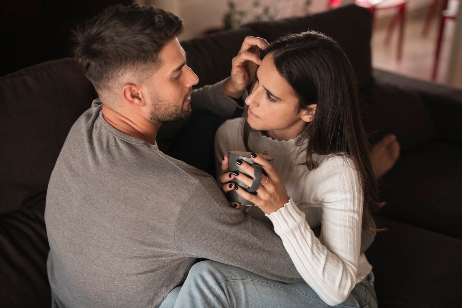 a couple sitting on a couch facing each other, embracing and talking
