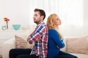 A couple sitting back-to-back with arms crossed on a couch, reflecting unresolved conflict and emotional distance in their relationship.