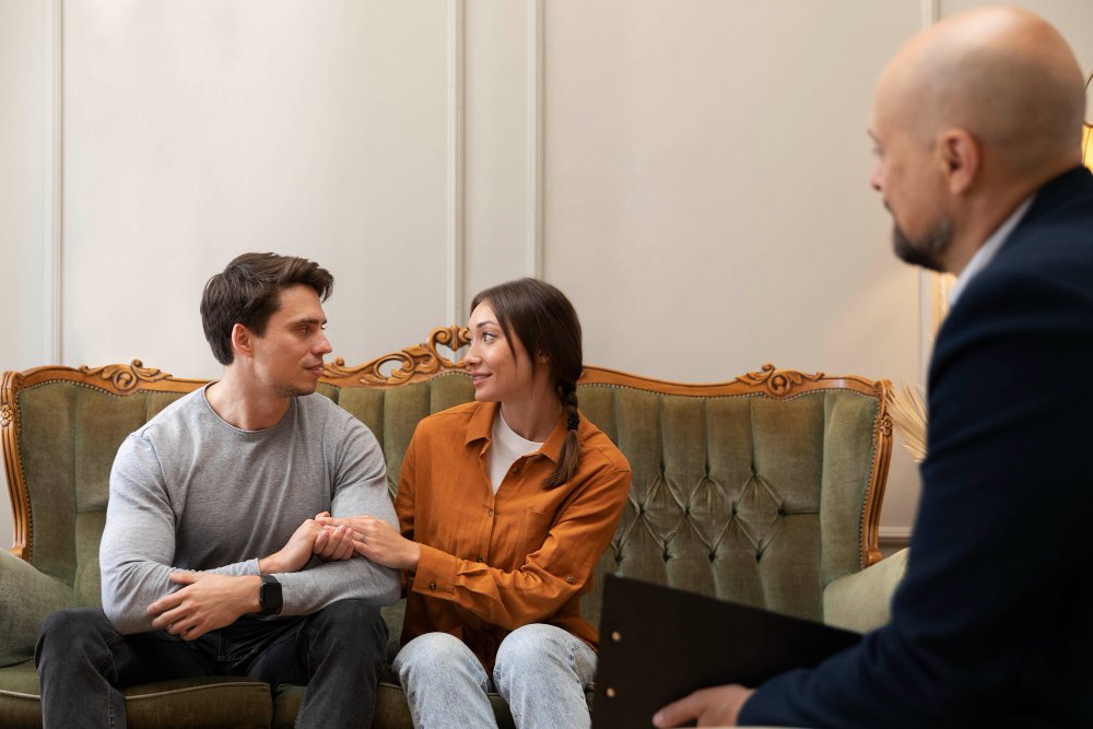 Couple seated closely during a therapy session, holding hands and making eye contact with therapist present, reflecting intimacy retreat for couples work