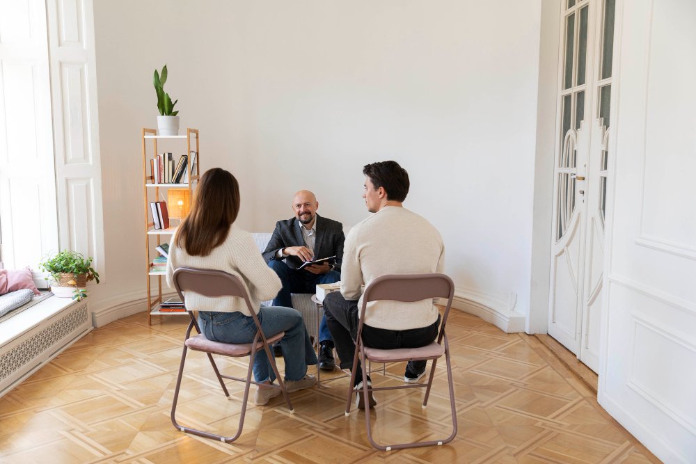 Couple seated across from therapist in a structured session, discussing relationship dynamics in a calm setting, reflecting intensive couples therapy work