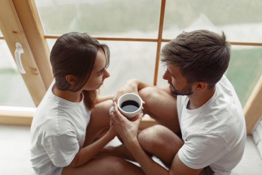 A couple sitting closely by a window sharing a quiet conversation, reflecting emotional intimacy and connection developed through an intimacy retreat for couples