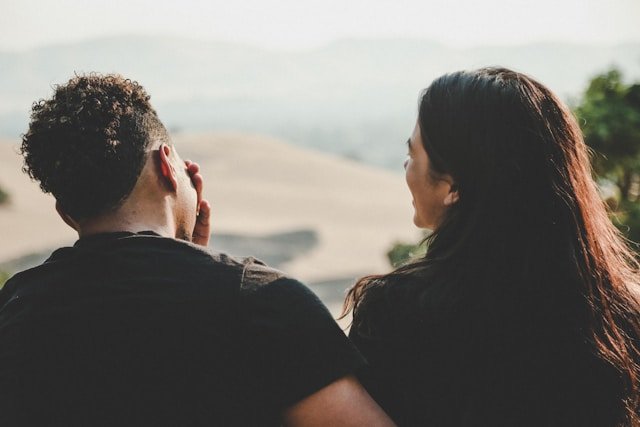 Couple in matching black shirts sitting close together in a park
