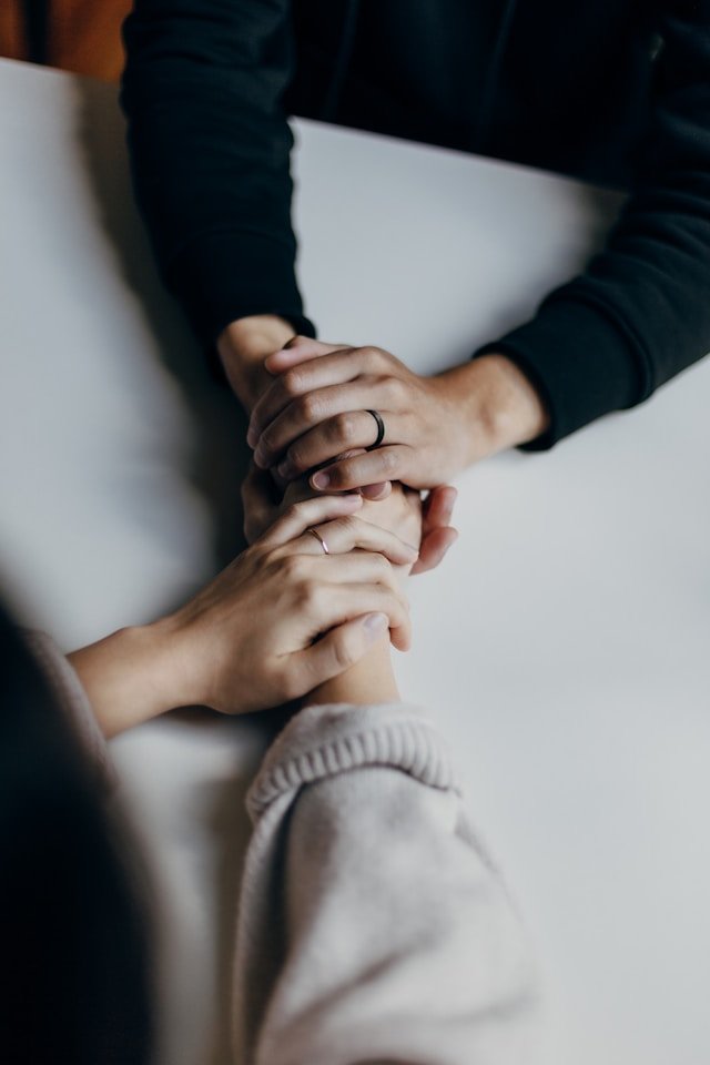 A married couple wearing their wedding rings gently holding hands 
