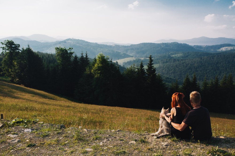 Couple sitting together on a green field, taking in mountain and nature views on a retreat.