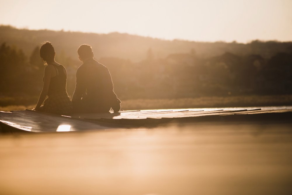 Couple sitting on a pier watching the sunset, a romantic moment during their couples retreat.