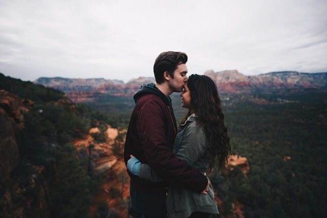 A man kissing his partner's forehead with mountains behind them, representing the closeness couples carry home from a retreat 