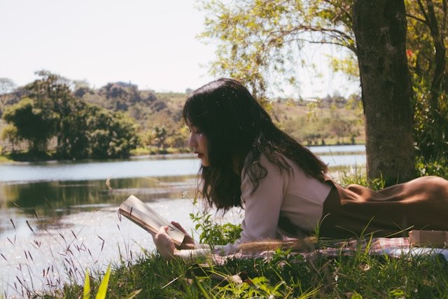 A woman reading beside the water, representing the personal reinvestment in identity that helps parents manage the empty nest