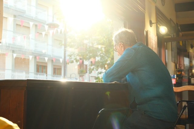 A man at a sunlit window in a quiet solitude, reflecting the restlessness and loss of purpose that empty nest syndrome brings 
