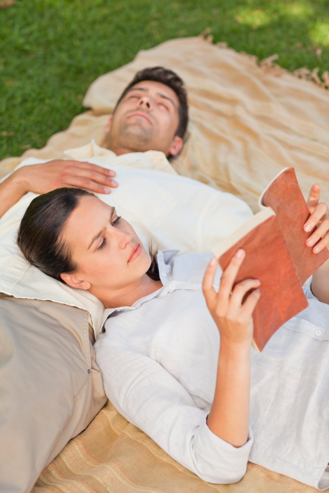 A couple relaxing on a blanket outdoors, one reading, showing do couples retreats work.
