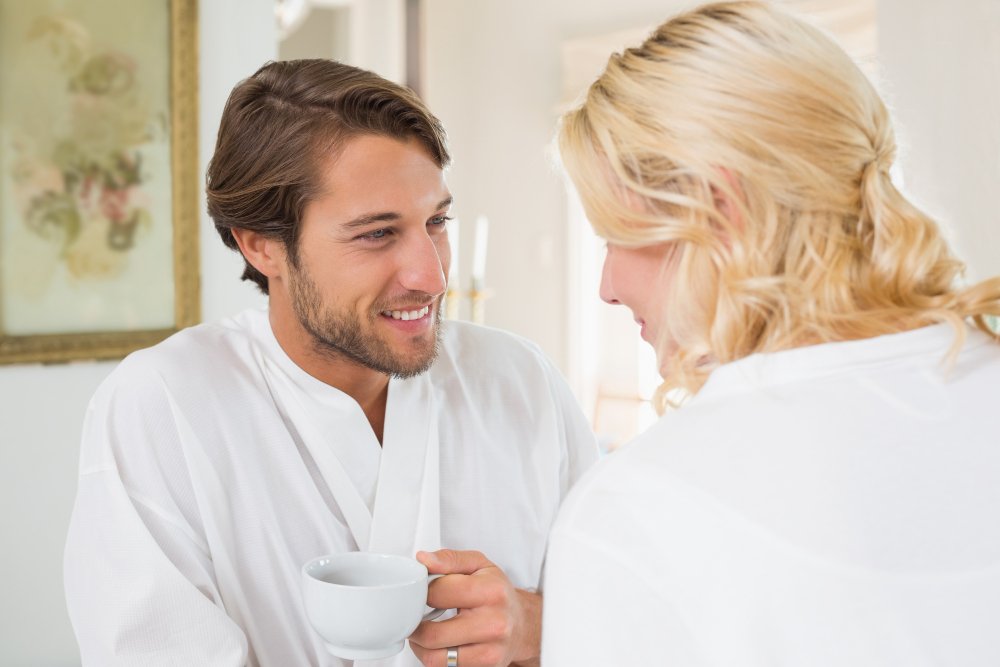 A couple in robes smiling over coffee, showing how to prepare for couples therapy.
