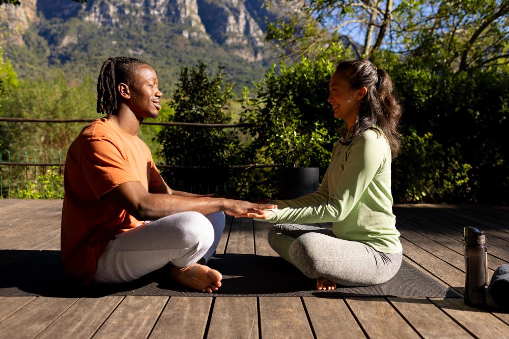 A couple sitting cross-legged outdoors holding hands, learning how to prepare for couples therapy.