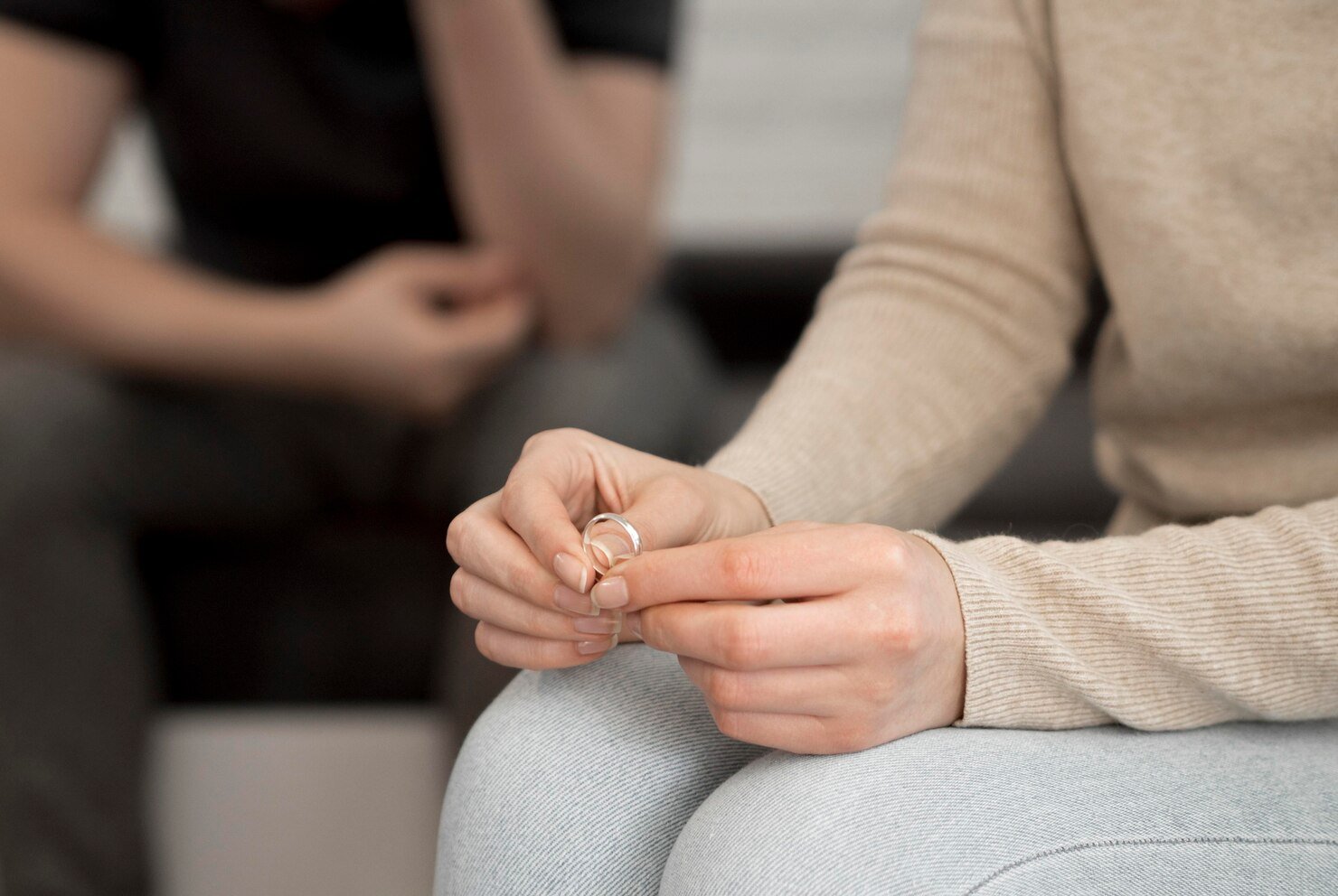 Couples therapy: woman holds wedding ring while partner crosses arms behind her