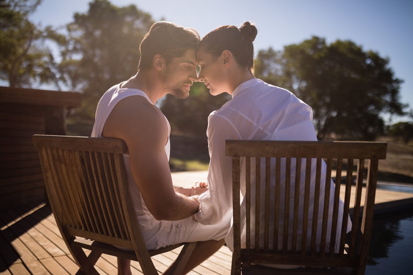 Couples retreat moment: pair sits forehead to forehead on deck at sunset