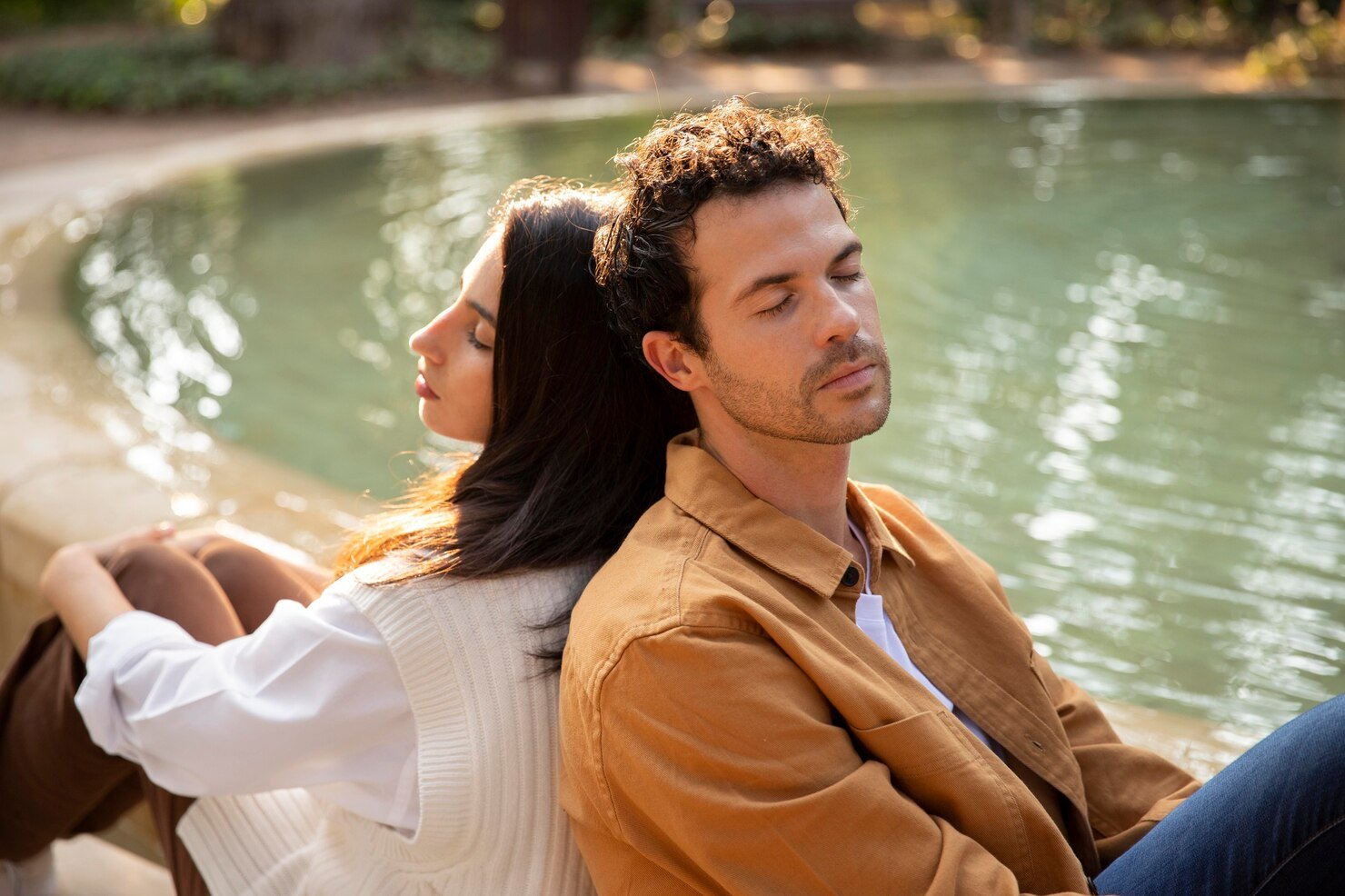 Couples retreat reflection: pair sits back to back with eyes closed by a pond